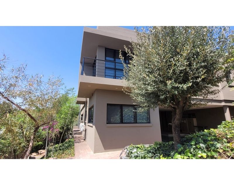 A modern two-story office building exterior featuring a balcony with metal railings, large windows, and landscaped surroundings.