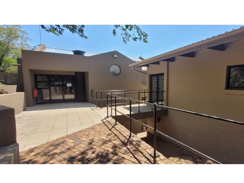 Exterior view of the office building featuring a paved courtyard, metal access ramp with railings, and modern architectural design elements.