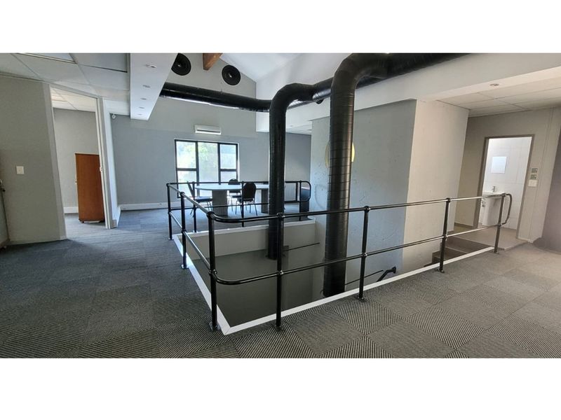 Open-plan office mezzanine level featuring industrial-style exposed ducting, carpeted flooring, and a metal safety railing overlooking the lower level.