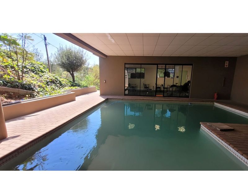 Covered indoor swimming pool area with brick paving, adjacent to an office space with large glass sliding doors.