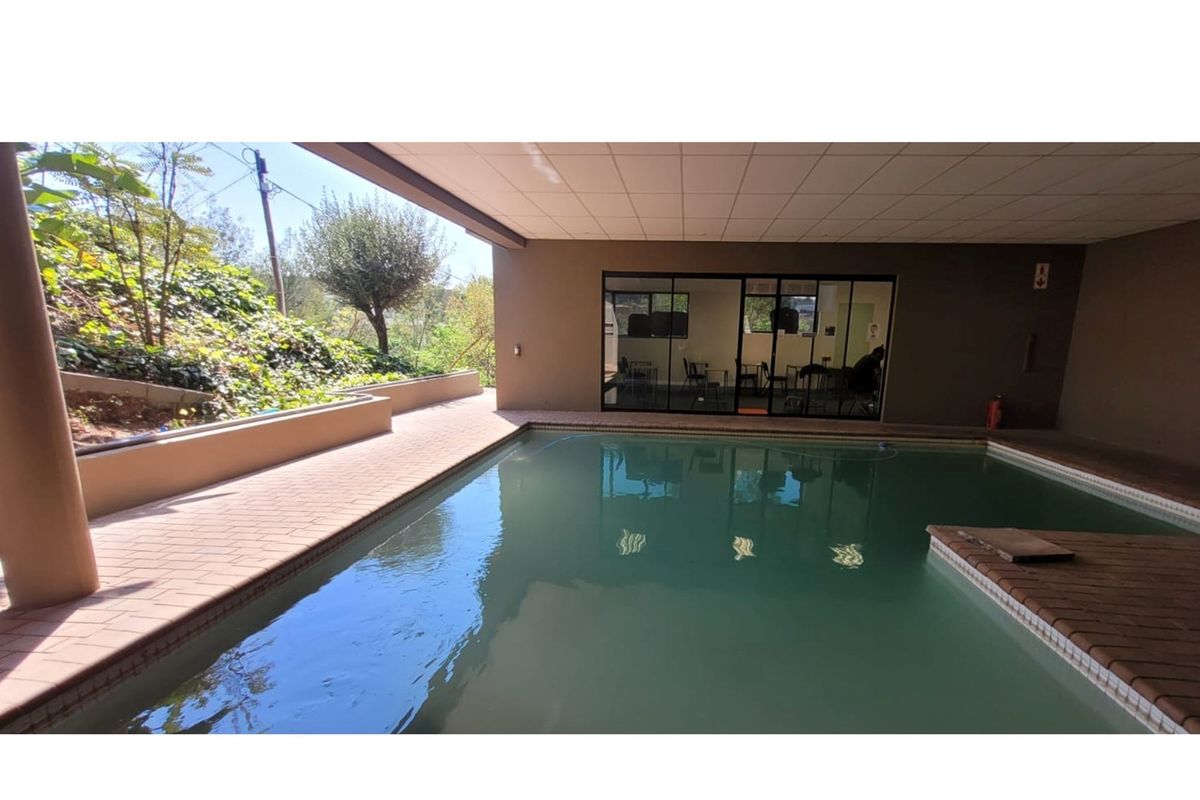 Covered indoor swimming pool area with brick paving, adjacent to an office space with large glass sliding doors.