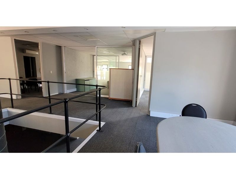 A functional office space featuring carpeted flooring, glass partition walls, and a mezzanine-style layout with black metal safety railings.