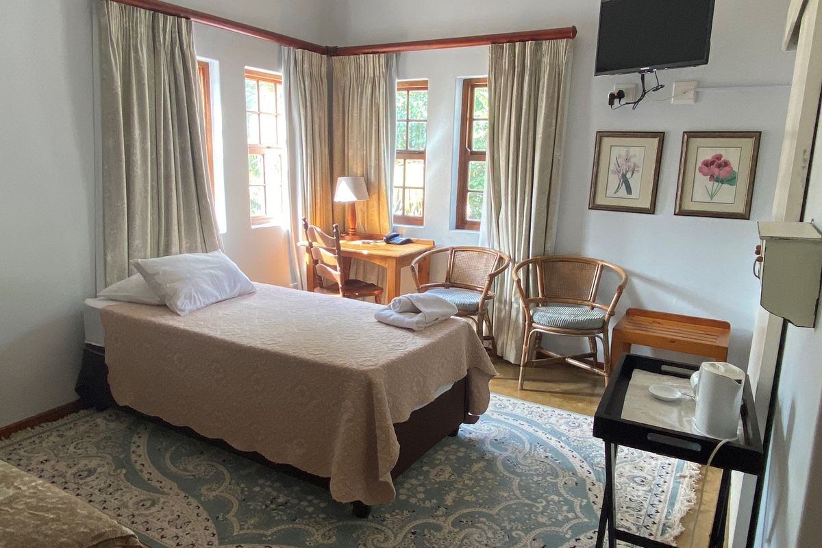 A cozy bedroom featuring timber-framed windows, wooden curtain rods, and neutral wall finishes, providing a comfortable and functional living space.