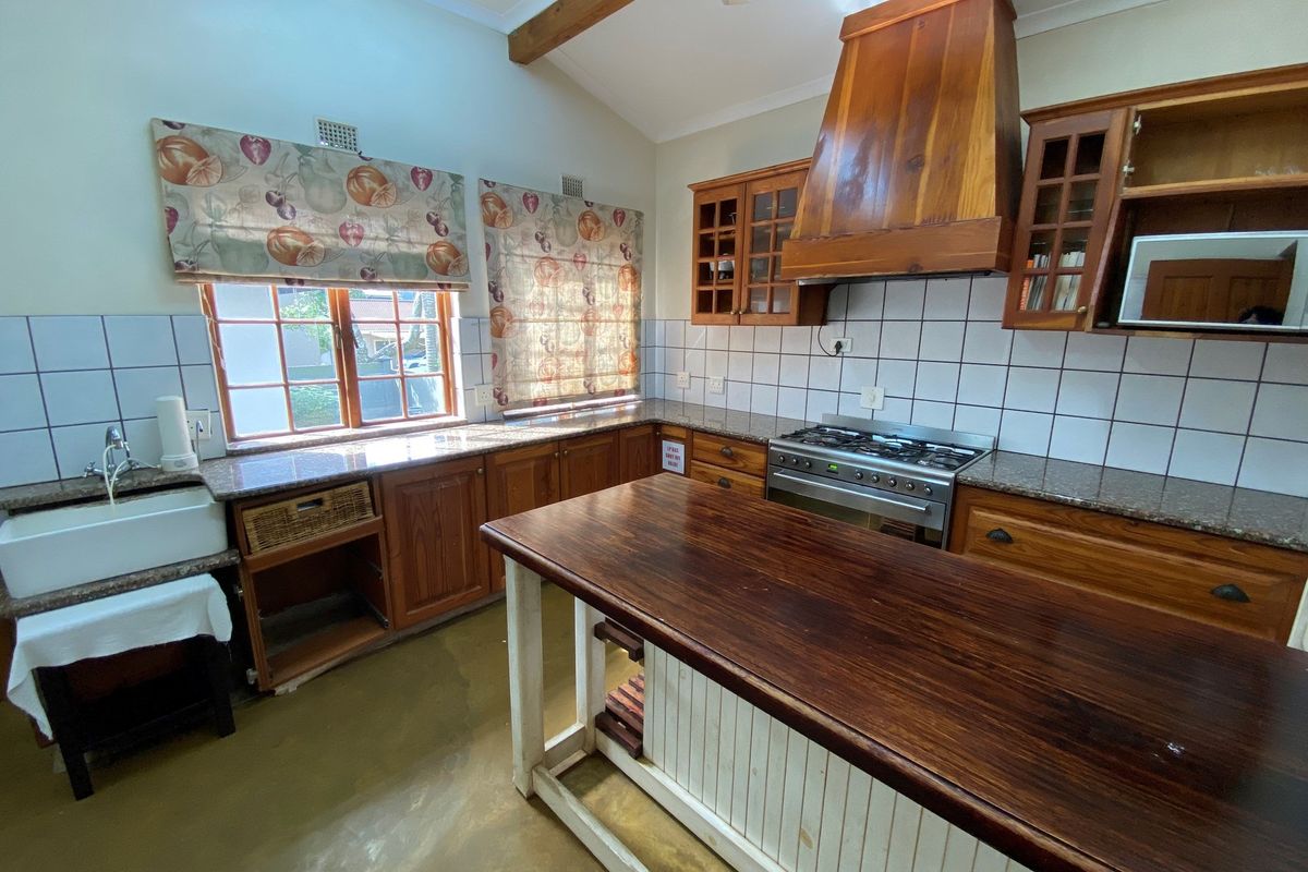 A rustic kitchen featuring wooden cabinetry, a built-in extractor hood, granite countertops, a farmhouse-style sink, and a central wooden island.