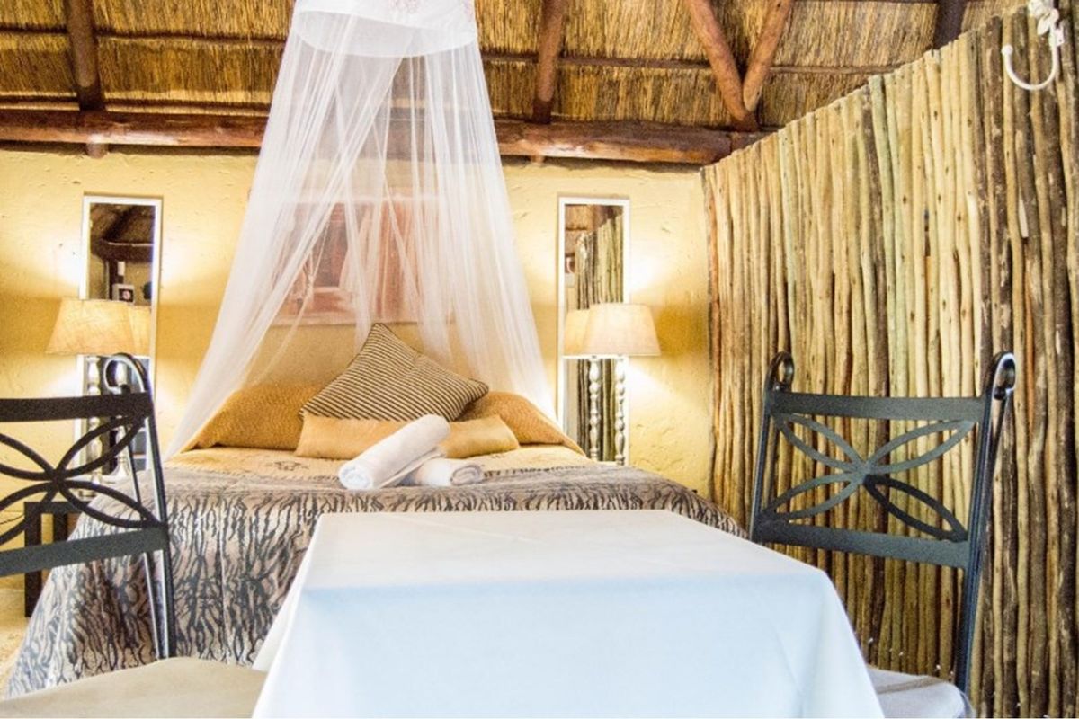 A rustic bedroom featuring a traditional thatched roof with exposed timber rafters and a unique timber pole feature wall.