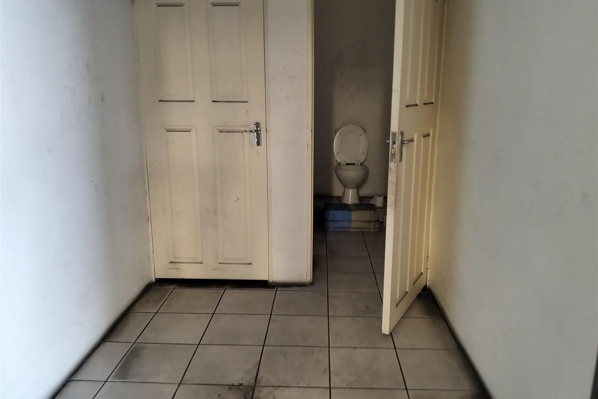 A small, utilitarian restroom area featuring tiled flooring and basic door fixtures, currently showing significant signs of wear and heavy soiling.