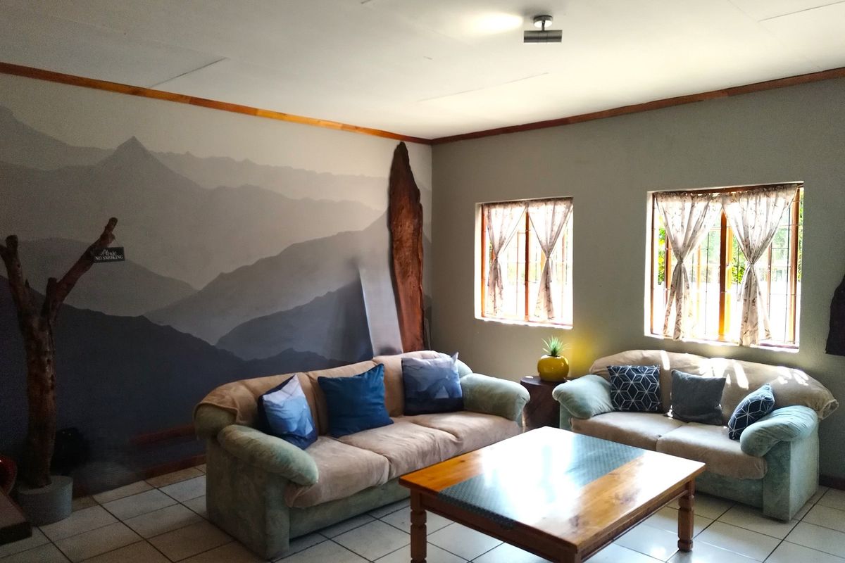 A living room area featuring tiled flooring, large windows with security bars, and a decorative mountain-themed feature wall.