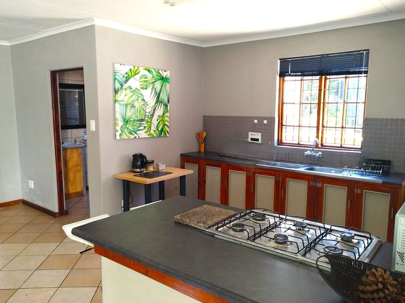 A functional kitchen featuring a central island with a built-in gas hob, dark countertops, wooden cabinetry, and a tiled backsplash.