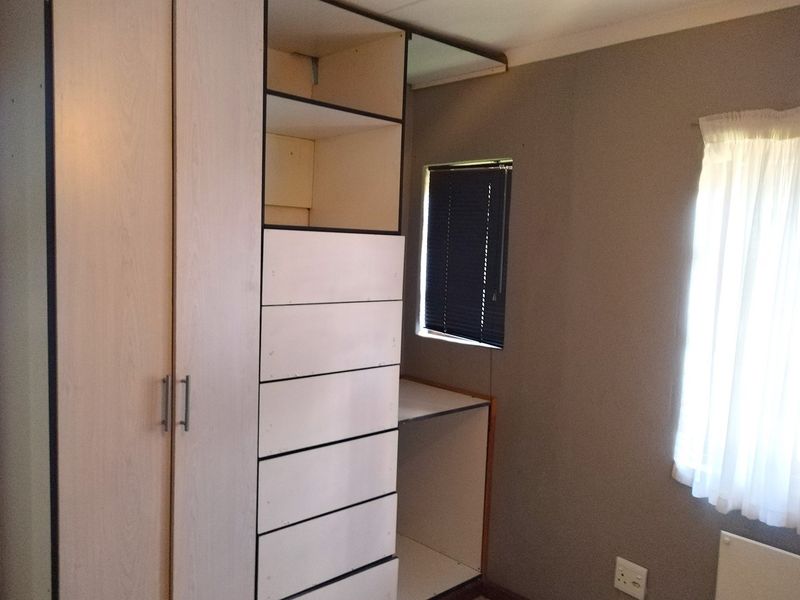 A bedroom featuring built-in light wood cabinetry with integrated shelving and drawers, alongside a window with fitted blinds.