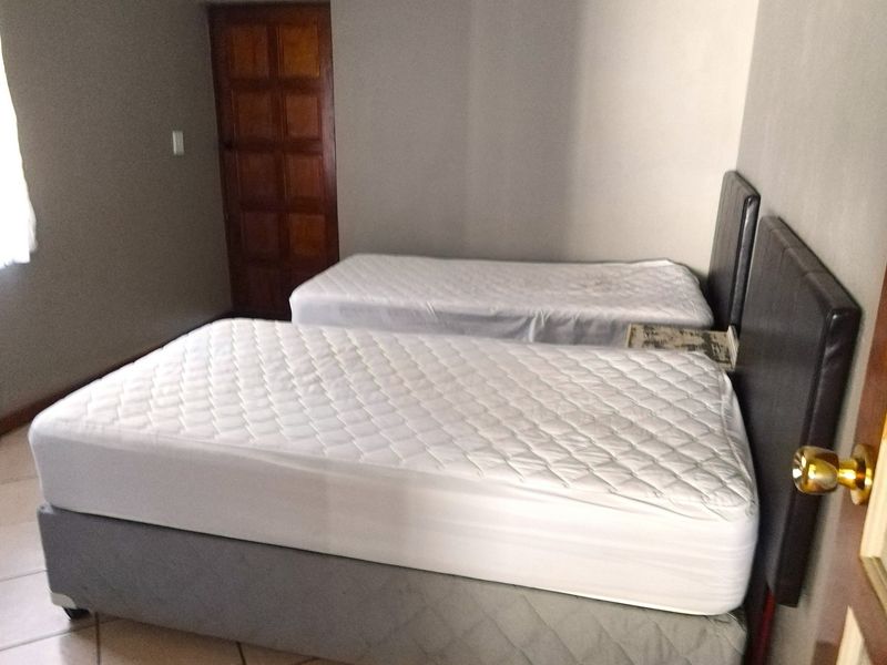 A bedroom featuring tiled flooring and a wooden door, currently configured with two single beds.
