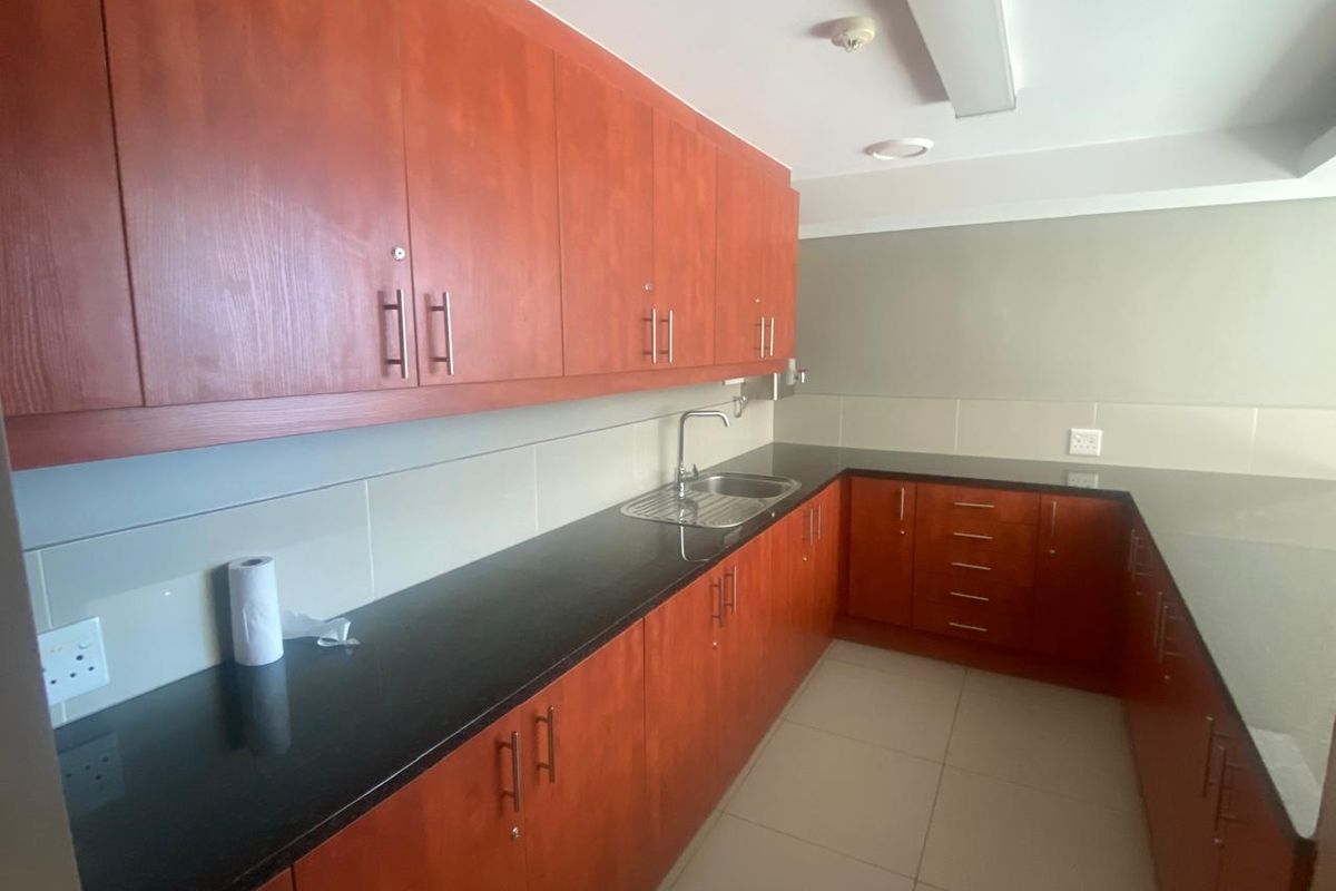 A functional office kitchenette featuring cherry wood cabinetry, dark granite countertops, a stainless steel sink, and tiled flooring.