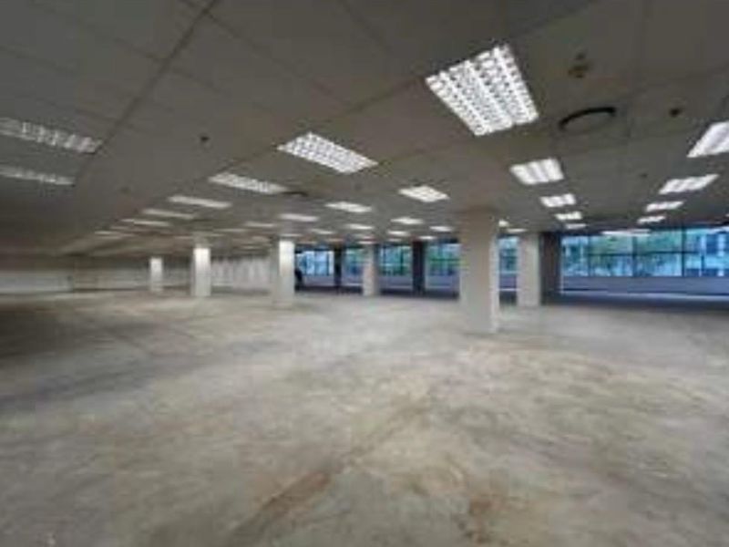A large, open-plan commercial retail space featuring a suspended ceiling with recessed lighting, concrete flooring, and expansive windows providing natural light.