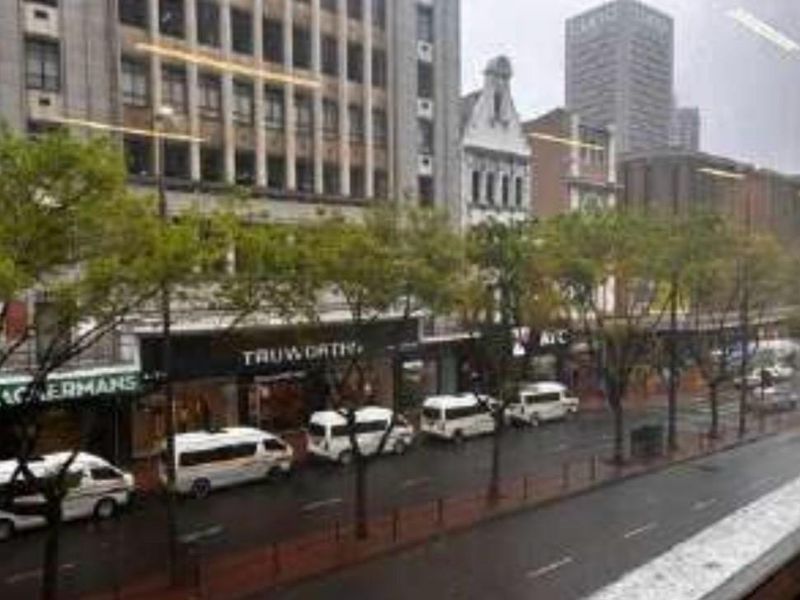 An elevated street-level view of a busy urban commercial district featuring multiple retail storefronts and street-side parking.