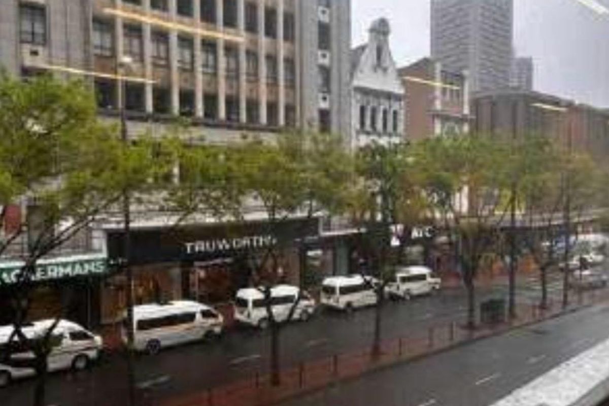 An elevated street-level view of a busy urban commercial district featuring multiple retail storefronts and street-side parking.
