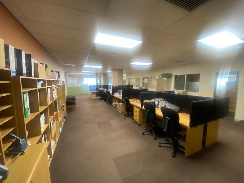 Open-plan office space featuring partitioned workstations, built-in shelving units, recessed ceiling lighting, and carpeted flooring.