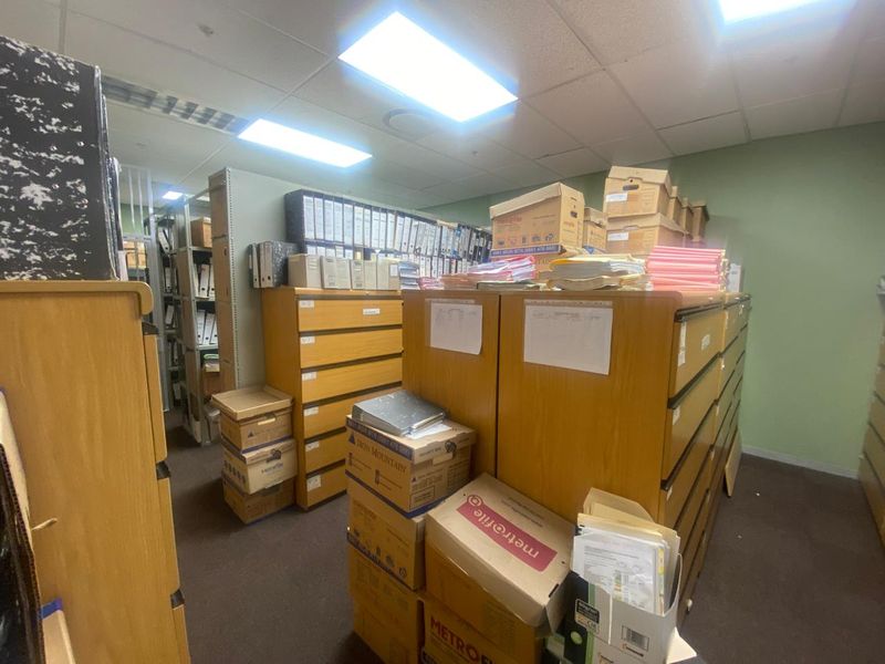 A functional office storage area featuring suspended ceiling tiles, recessed lighting, and carpeted flooring, currently utilized for document archiving.