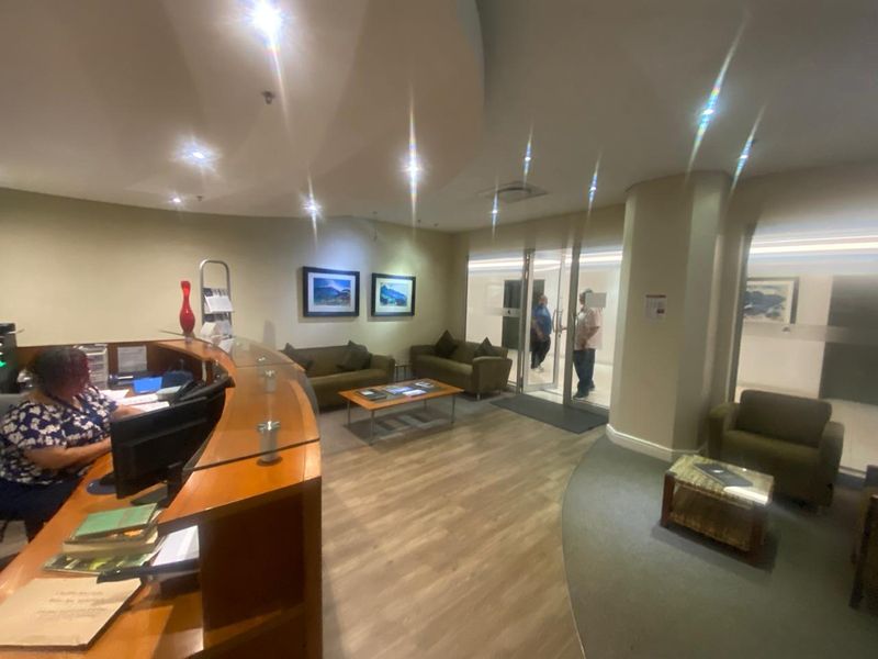A professional office reception area featuring a curved built-in desk, recessed lighting, and glass entry doors with a welcoming waiting space.