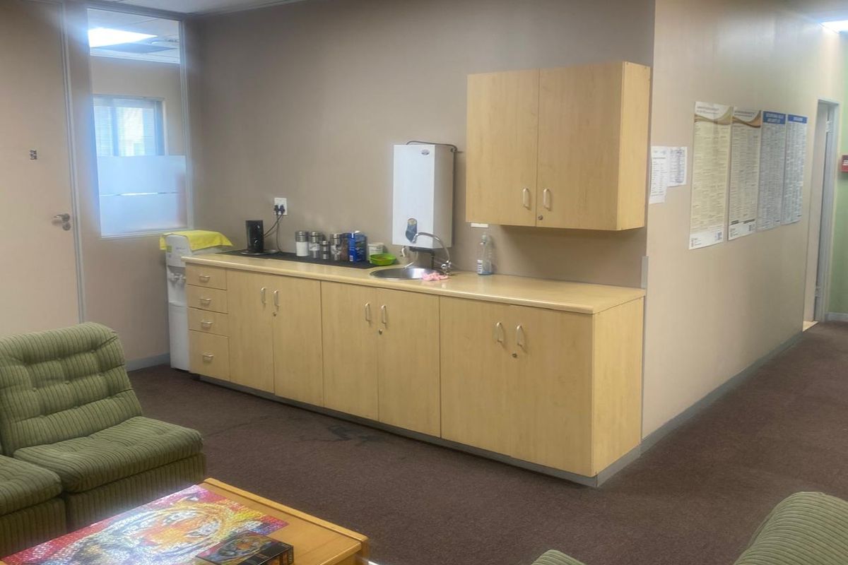 A functional office kitchenette featuring light wood cabinetry, a sink, and a wall-mounted water heater, providing a convenient break area for staff.