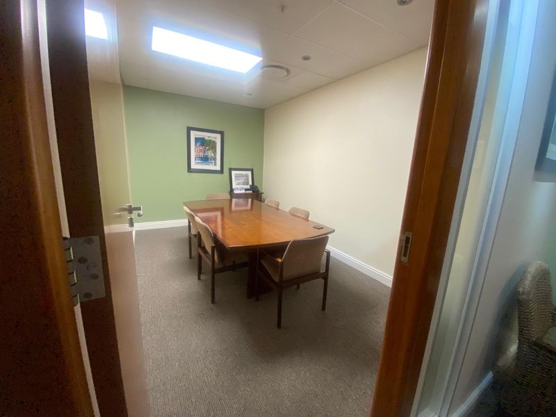 A functional office meeting room featuring carpeted flooring, suspended ceiling tiles with recessed lighting, and a neutral color palette.