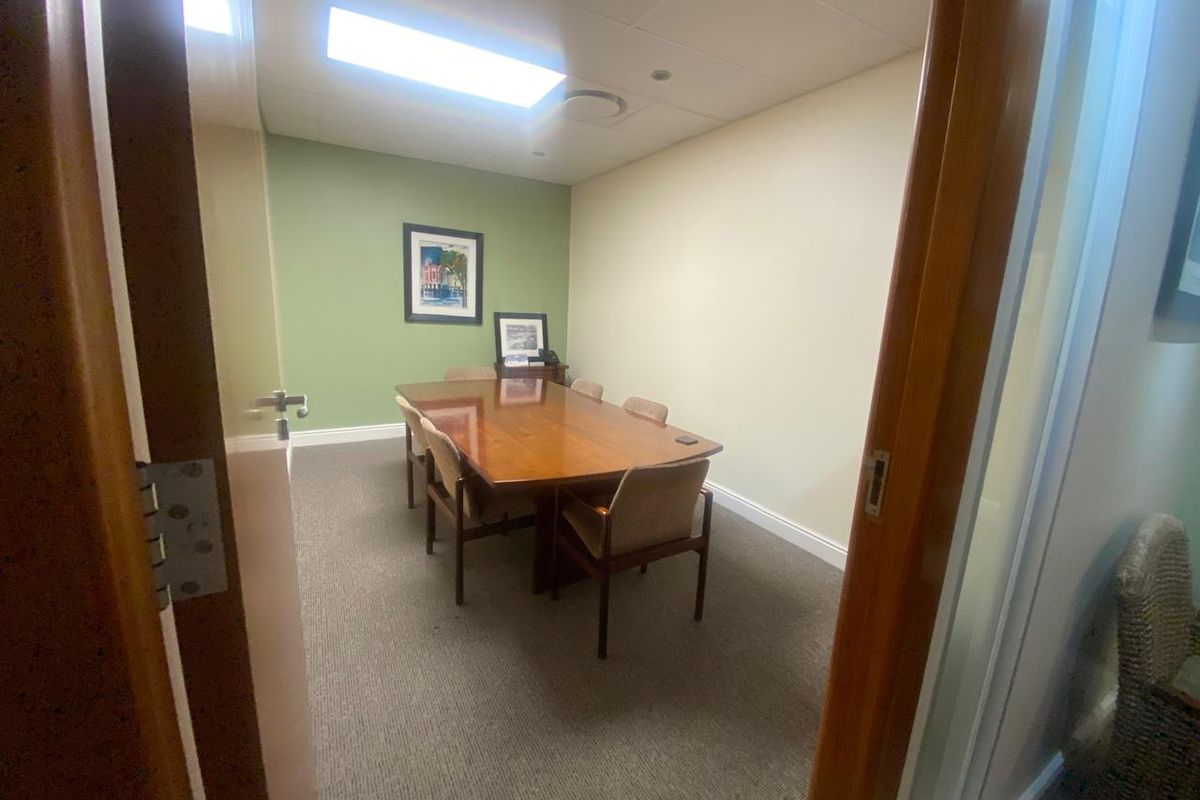 A functional office meeting room featuring carpeted flooring, suspended ceiling tiles with recessed lighting, and a neutral color palette.