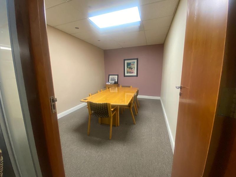 A functional office meeting room featuring carpeted flooring, a suspended ceiling with recessed lighting, and neutral wall finishes.