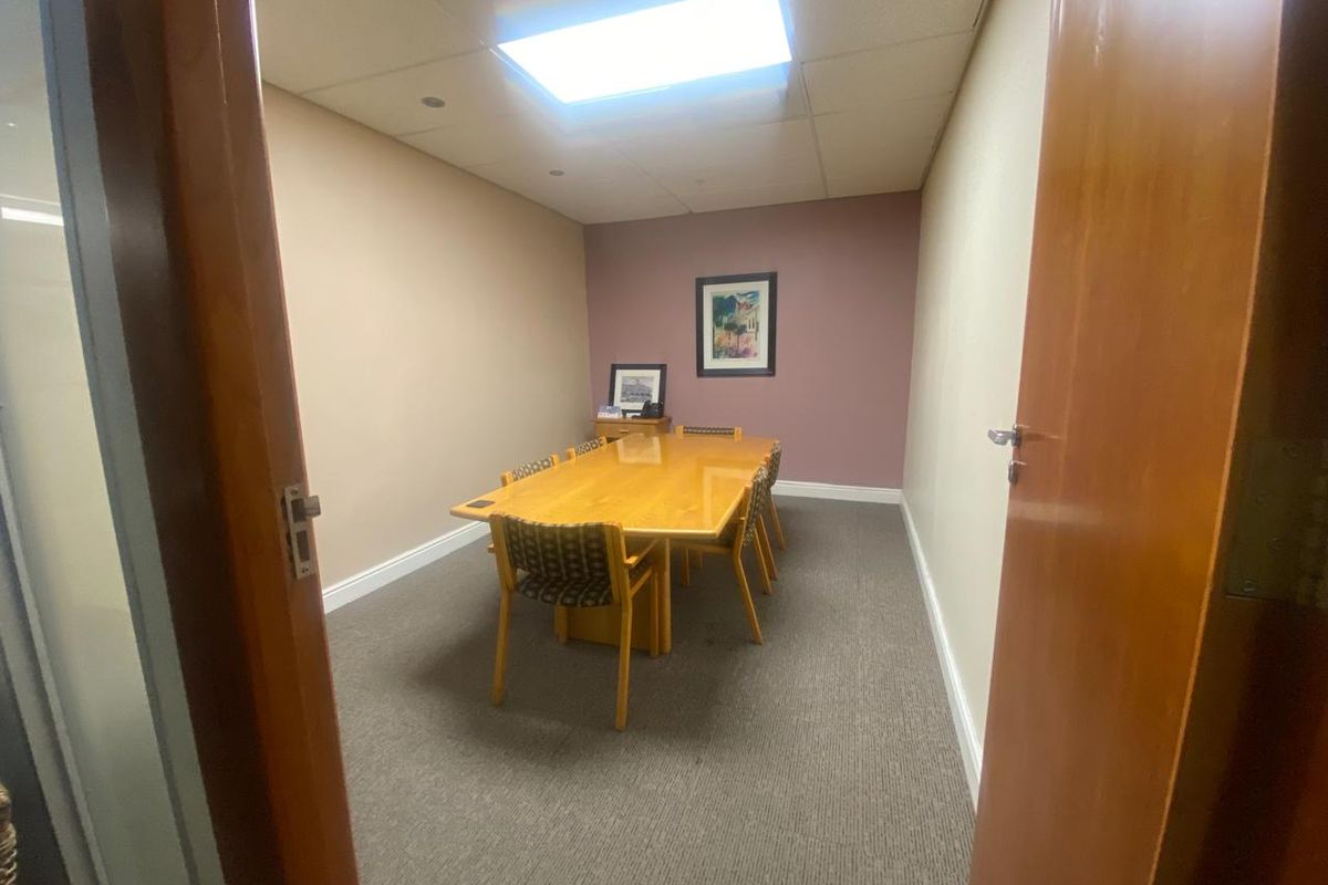 A functional office meeting room featuring carpeted flooring, a suspended ceiling with recessed lighting, and neutral wall finishes.