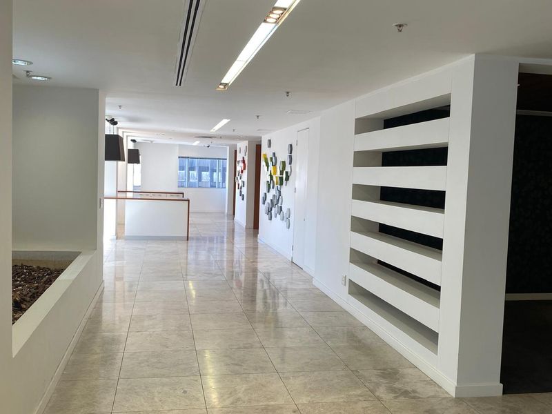 A spacious, modern office corridor featuring polished tiled flooring, recessed ceiling lighting, and a prominent built-in shelving unit.