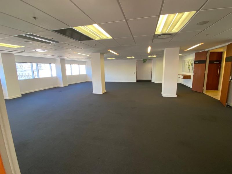 Spacious open-plan office area featuring a suspended ceiling, recessed lighting, and large windows providing ample natural light.