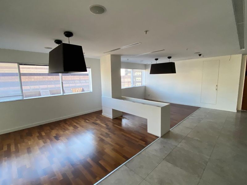 Spacious open-plan office area featuring a mix of hardwood and tiled flooring, large windows for natural light, and modern recessed ceiling lighting.