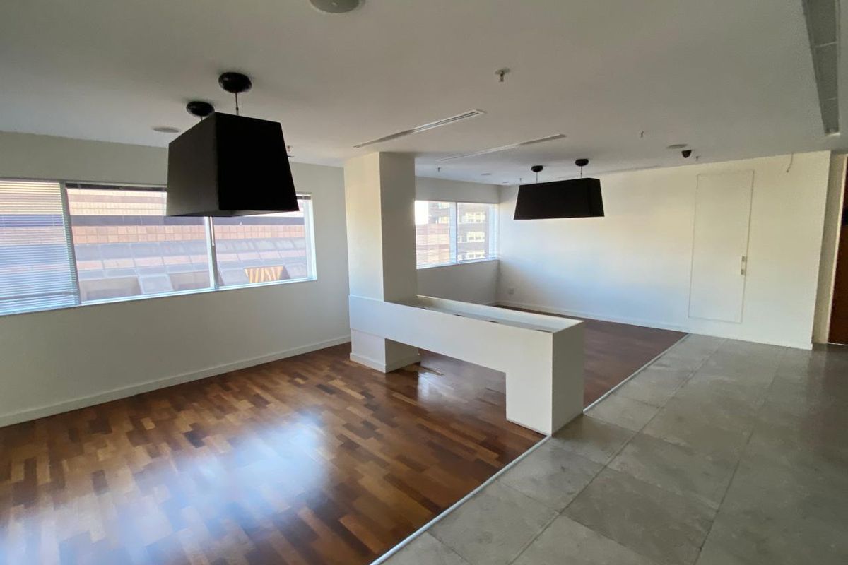 Spacious open-plan office area featuring a mix of hardwood and tiled flooring, large windows for natural light, and modern recessed ceiling lighting.