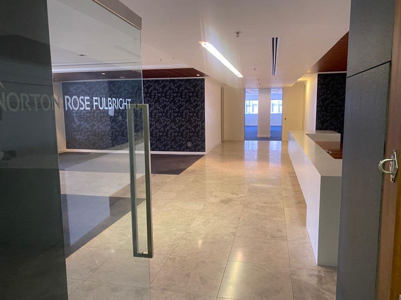 A professional office entrance featuring a glass door, polished stone flooring, a built-in reception desk, and modern recessed lighting.