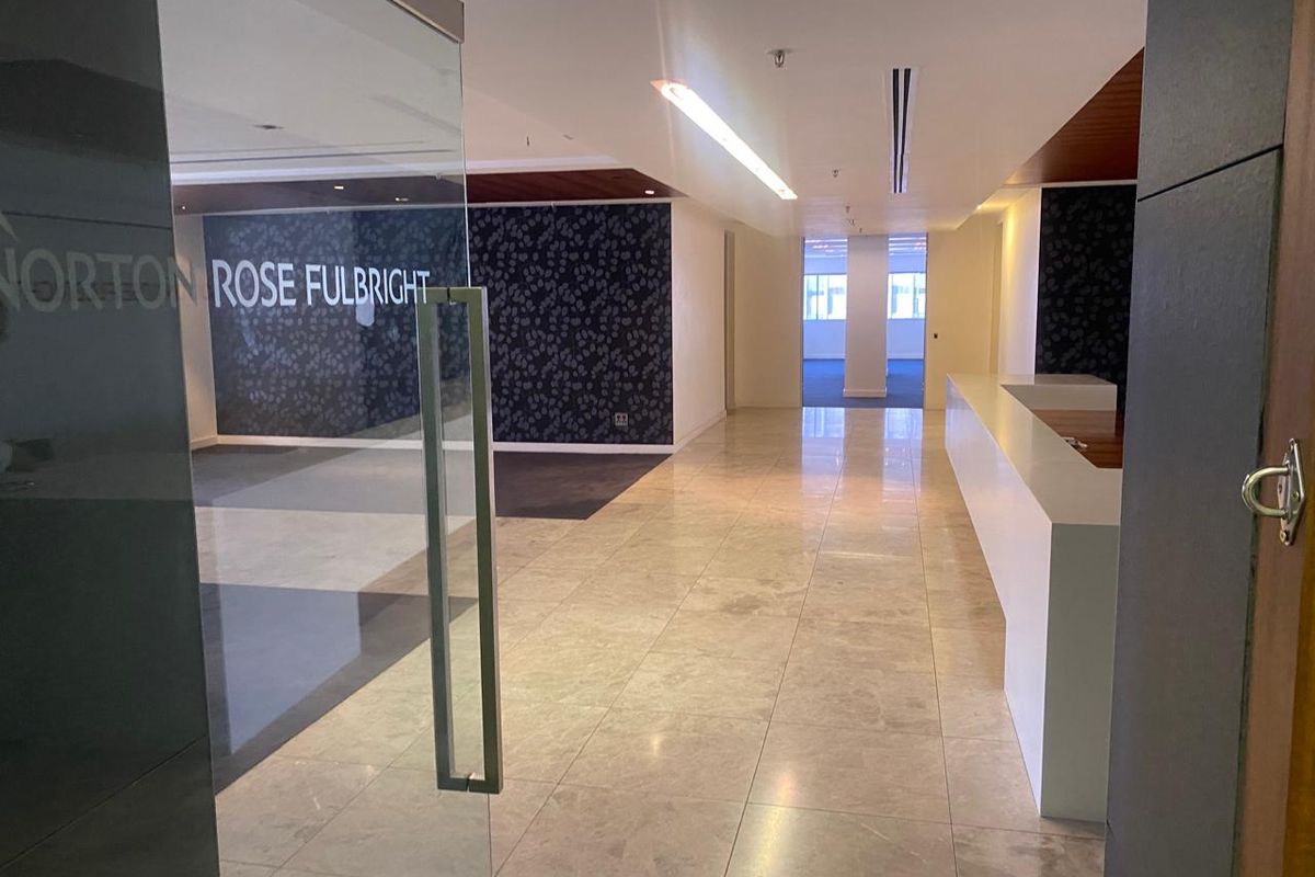 A professional office entrance featuring a glass door, polished stone flooring, a built-in reception desk, and modern recessed lighting.