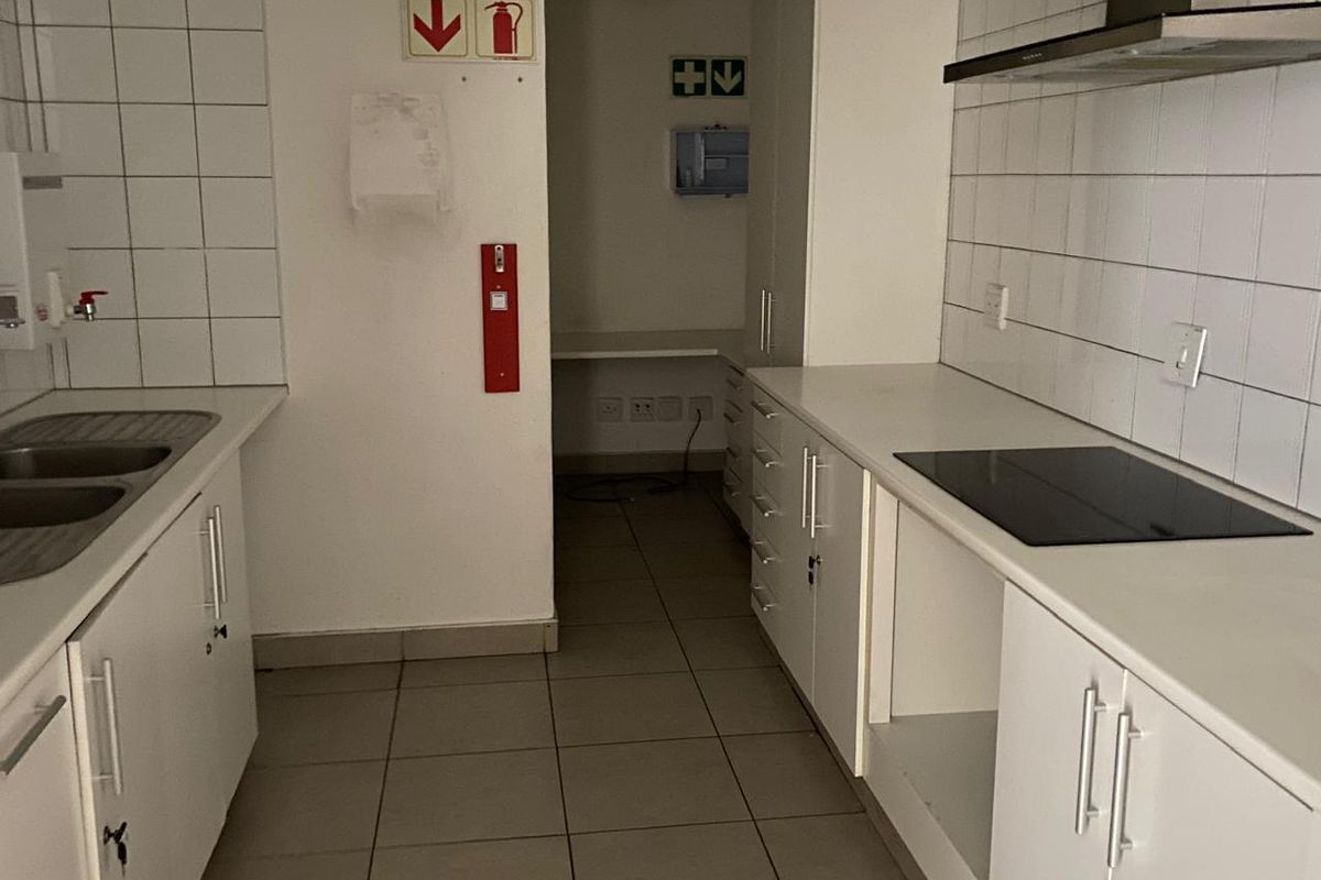 Functional office kitchen area featuring built-in cabinetry, a double sink, ceramic hob, extractor fan, and tiled finishes throughout.