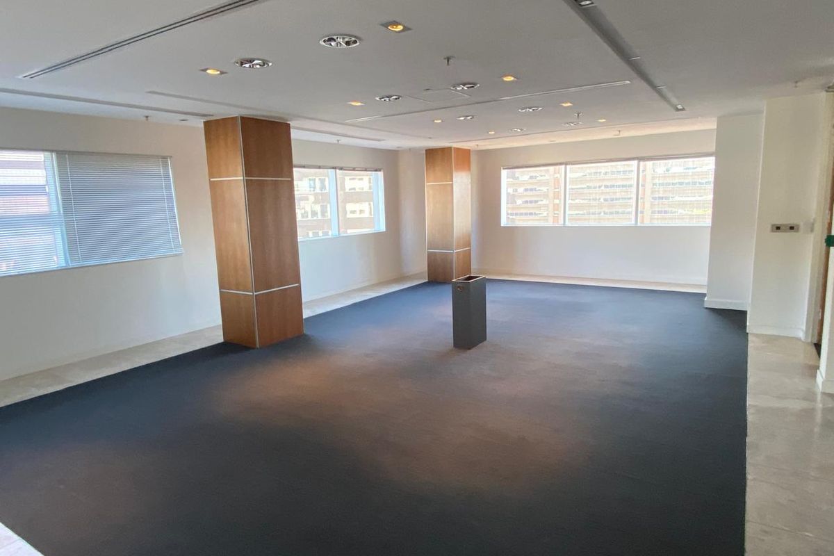 A spacious, open-plan office area featuring modern recessed lighting, wood-clad support columns, and large windows providing ample natural light.