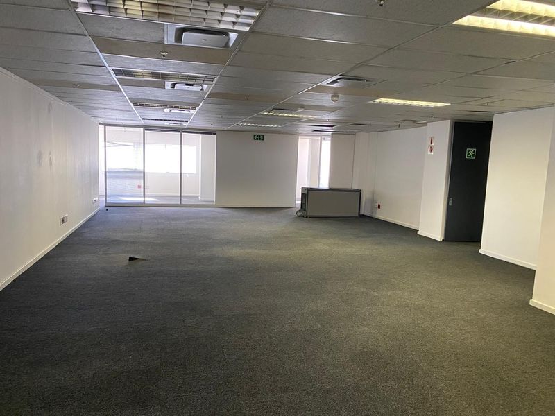 A spacious, vacant open-plan office area featuring a suspended ceiling, recessed lighting, and large sliding glass doors providing natural light.