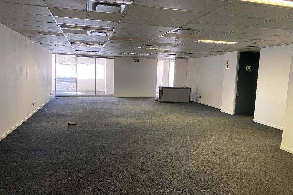 A spacious, vacant open-plan office area featuring a suspended ceiling, recessed lighting, and large sliding glass doors providing natural light.