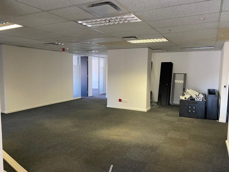 An open-plan office space featuring carpet tiles, a suspended ceiling with recessed lighting, and glass partition doors leading to adjacent rooms.