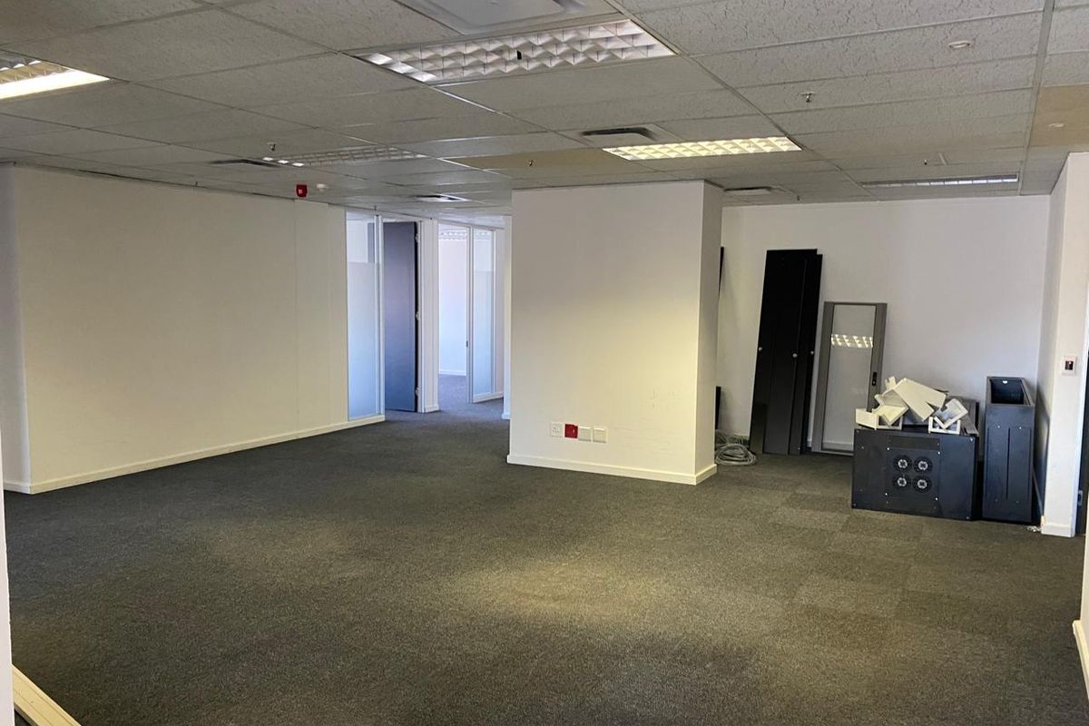 An open-plan office space featuring carpet tiles, a suspended ceiling with recessed lighting, and glass partition doors leading to adjacent rooms.