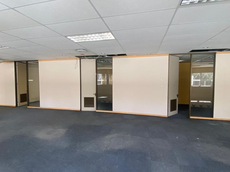An empty office space featuring glass partitions, suspended ceilings with recessed lighting, and carpeted flooring, currently requiring maintenance to ceiling panels and wiring.