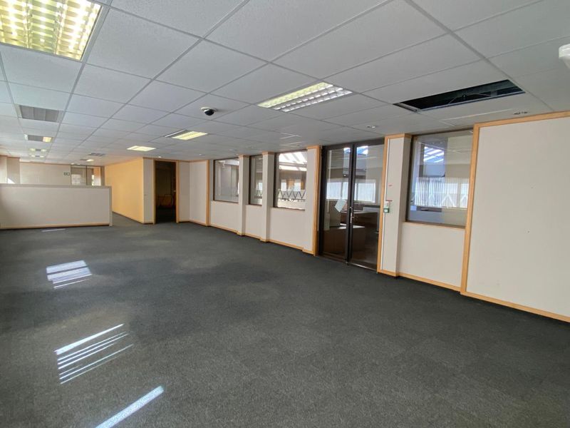 An open-plan office space featuring suspended ceilings, recessed lighting, glass partitions, and carpet flooring, currently vacant and ready for customization.