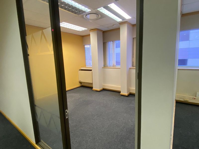 A vacant office space featuring carpeted flooring, suspended ceiling with integrated lighting, and a glass partition door.