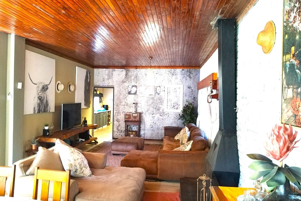 A cozy living room featuring a wood-paneled ceiling, a built-in fireplace, and an open-plan layout leading to an adjacent kitchen area.