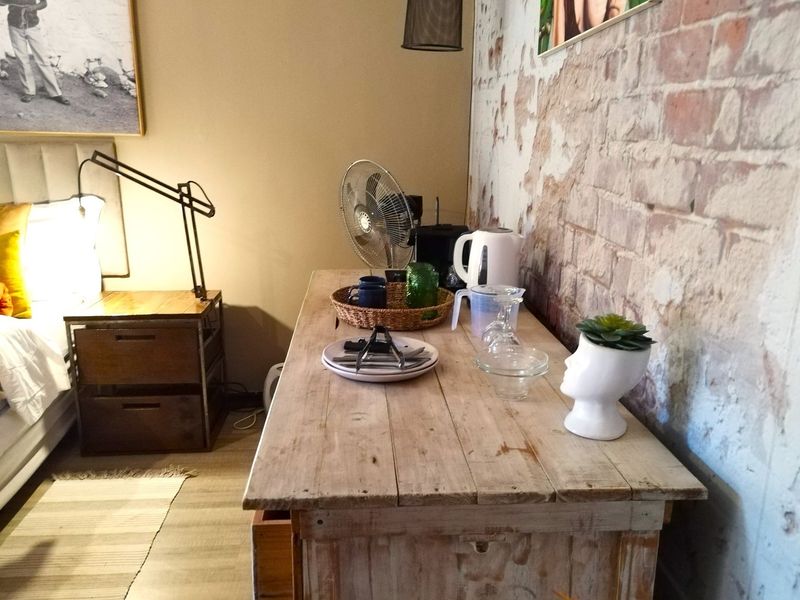 A bedroom interior featuring a rustic wooden console table and an exposed brick feature wall, creating a warm and textured atmosphere.
