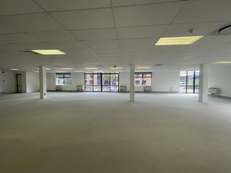 A spacious, open-plan office area featuring a suspended ceiling, recessed lighting, and large windows providing ample natural light and exterior views.