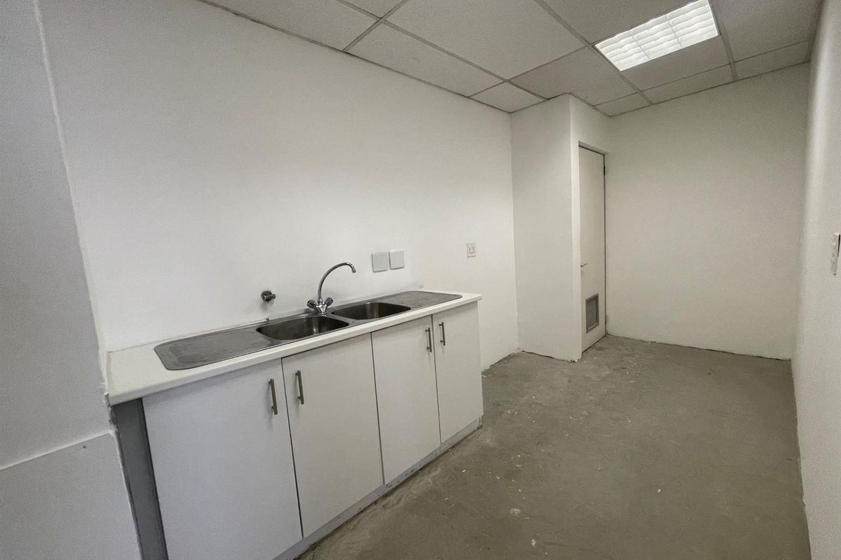 A small office kitchenette featuring white cabinetry, a stainless steel sink, and a drop ceiling, currently awaiting final flooring installation.