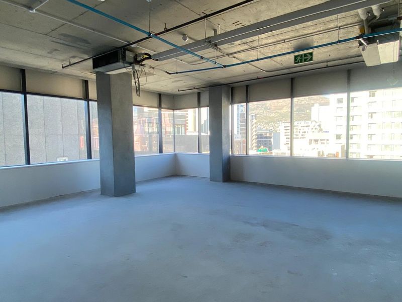 An open-plan office space featuring floor-to-ceiling windows, exposed concrete structural elements, and industrial-style ceiling infrastructure, offering a blank canvas for custom fit-out.