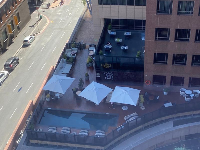 An elevated view of an outdoor terrace featuring a swimming pool, wooden decking, and integrated seating areas adjacent to a commercial office building.