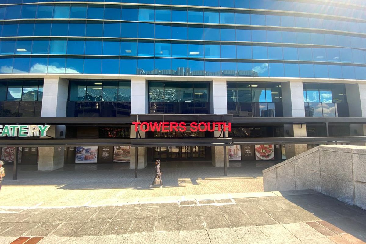 Front elevation of the Towers South office building featuring a modern glass facade, paved entrance plaza, and prominent commercial signage.