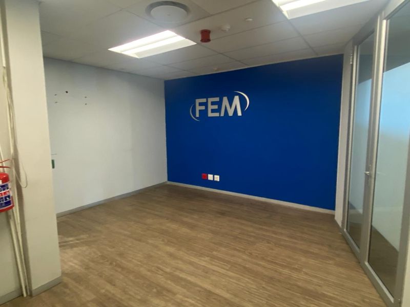 A vacant office space featuring laminate flooring, a suspended ceiling with recessed lighting, and a prominent blue accent wall with glass partition entry.