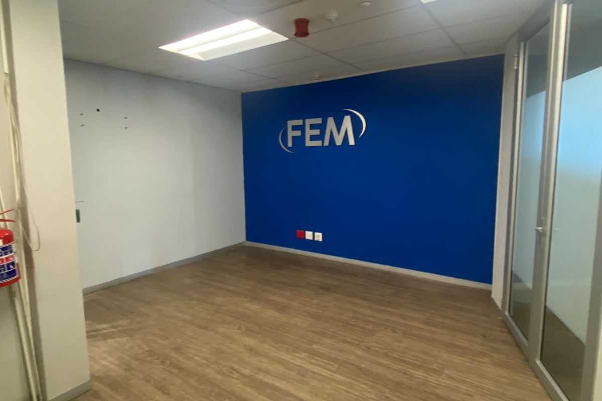 A vacant office space featuring laminate flooring, a suspended ceiling with recessed lighting, and a prominent blue accent wall with glass partition entry.